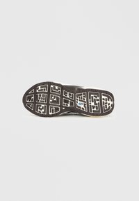 Černá gumová podrážka boty s texturovaným vzorem běhounu, obsahující geometrické motivy a logo uprostřed, na bílém pozadí.