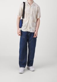 Kortsleeve cremet skjorte med paisley mønster, parret med løse blå denim jeans. Tilbehøret inkluderer en lille blå taske og hvide sneakers på fødderne.