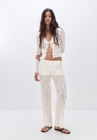Häkelspitzen-Zweiteiler in Off-White, bestehend aus einem cropped Top mit vorderem ZTie und lockeren Hosen, mit einem durchsichtigen, strukturierten Muster.