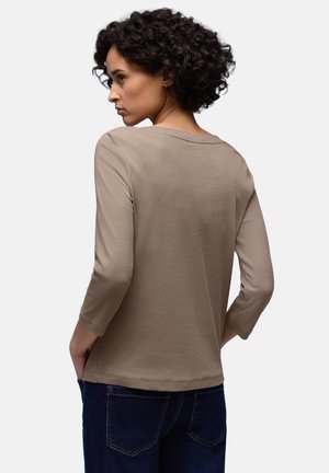 Beżowa prążkowana koszula z rękawami do połowy ramienia, posiada szeroki dekolt, luźny krój i jest zestawiona z ciemnymi jeansami.