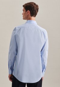 Light blue, long-sleeve shirt with a button-up collar, rounded hem, and visible stitching. Cotton blend fabric with a smooth texture.