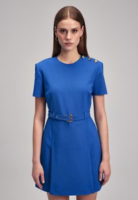 Blue fitted dress with short sleeves, round neck, gold button accents on the shoulder, and a waist belt with a buckle detail.