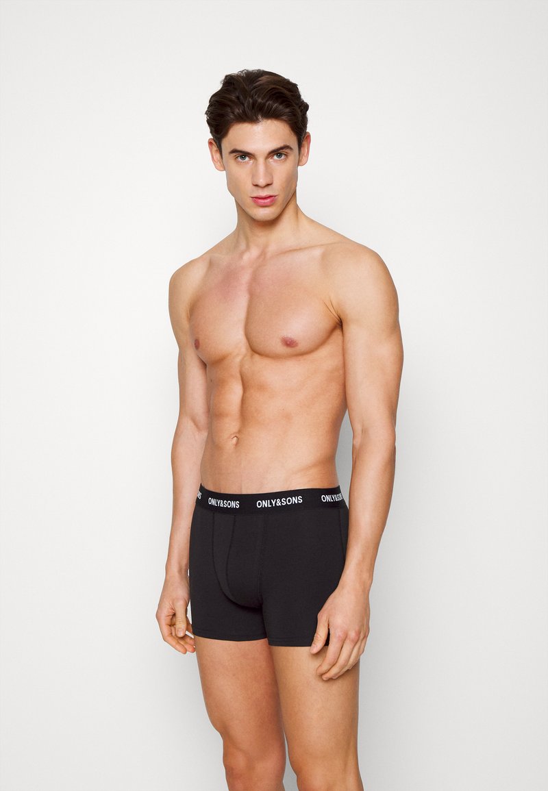 Schwarze Boxershorts mit elastischem Bund, der ein weißes Markenlogo zeigt. Der Stoff wirkt weich und glatt und schmiegt sich eng an den Körper.
