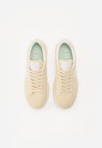 Scarpe da ginnastica beige con tomaia in rete, tessuto testurizzato, accenti bianchi e soletta verde. Presentano punta rotonda e allacciatura tradizionale.