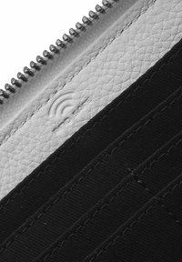 Tessuto nero con pelle bianca texturizzata, caratterizzato da una chiusura a zip e un logo in rilievo sottile sulla pelle. Cuciture a contrasto visibili.