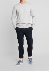 Jasnoszary sweter, granatowe chinosy, niebieskie zamszowe trampki z białymi podeszwami. Sweter ma okrągły dekolt i długie rękawy, spodnie mają podwinięte nogawki.