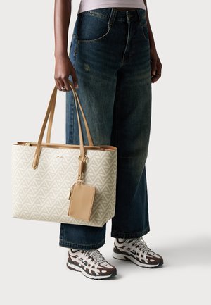 Bolso de tote de color beige con estampado y detalles en cuero, que presenta diseños geométricos, dos asas y un detalle de etiqueta de equipaje a juego.