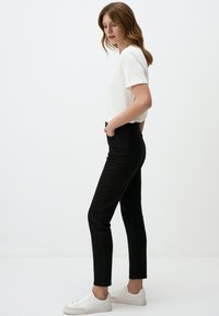 Czarne spodnie dżinsowe z wysokim stanem i dopasowanym krojem, z tylnymi kieszeniami i gładką fakturą. W połączeniu z białą koszulką z krótkim rękawem i białymi trampkami.