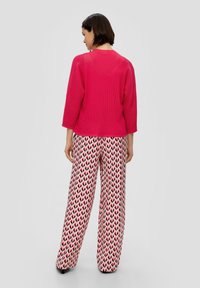 Helles pinkes geripptes Sweater mit drei Viertelärmeln, kombiniert mit weit geschnittenen Hosen in einem rosa und schwarzen Herzmuster. Glatte Textur.