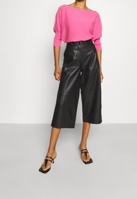 Fuchsia gestrickter Pullover mit weitem Ausschnitt, kombiniert mit hoch taillierten schwarzen Leder-Culottes und minimalistischen schwarzen Riemchensandalen.