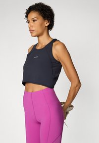 Top desportivo preto cortado com decote redondo, combinado com leggings rosa-choque de cintura alta com detalhes nas costuras.