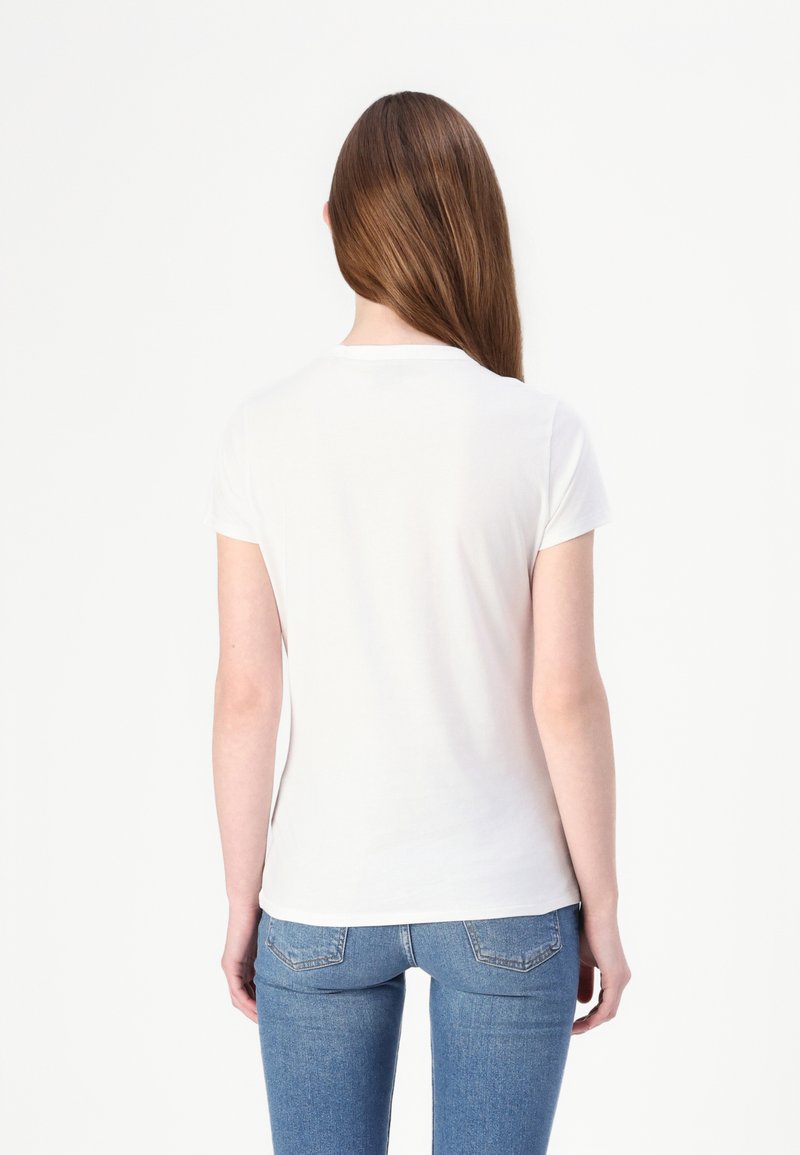 Weißes T-Shirt mit kurzen Ärmeln aus weicher Baumwolle, mit klassischem Rundhalsausschnitt und figurbetontem Schnitt, kombiniert mit blauen, eng anliegenden Jeans.