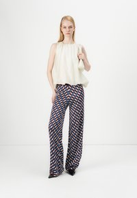 Haut sans manches de couleur claire avec une coupe ample, associé à un pantalon large à motifs présentant des formes géométriques en rouge, bleu et crème.