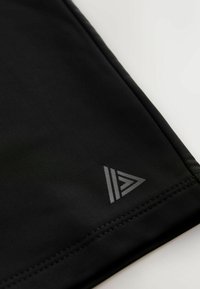 Tela negra con un pequeño logo triangular gris cerca de un dobladillo cosido, mostrado sobre un fondo blanco.