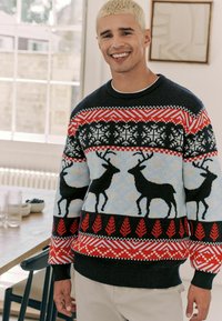 Pulover tricotat cu o bază bleumarin, modele festive roșii, negre și albe, inclusiv reni și fulgi de zăpadă, cu un guler și mansete ribotate.