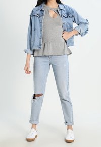 Jeansjacke mit Rüschenschultern, graues Peplum-Oberteil mit Schlüsselloch, ausgebleichte hellblaue Jeans und weiße Sneakers mit braunen Sohlen.