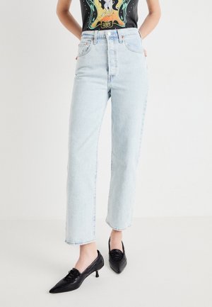 Personne portant un jean droit taille haute bleu clair, des chaussures à talons kitten noires à bouts pointus et un t-shirt noir graphique.