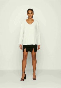 Blusa branca de manga longa com decote em V combinada com uma saia mini preta com fendas frontais, complementada por sandálias de salto alto pretas com tiras.