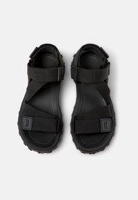 Sorte sandaler med justerbare stropper, en robust såle, teksturert fotseng og et enkelt kryss-design. Laget av slitesterke materialer.