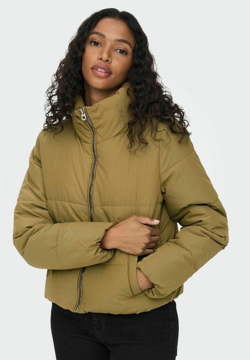 Chaqueta acolchada de color verde oliva con cuello alto, cremallera frontal y puños acanalados. La tela parece suave y ligera, adecuada para superponer.