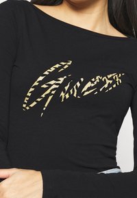 Svart långärmad tröja med en guldglittrig grafisk logotyp med tigerstrimmigt mönster. Materialet verkar mjukt och kroppsnära.