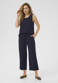 Top senza maniche blu navy abbinato a pantaloni larghi blu navy, entrambi realizzati in tessuto leggero; indossato con scarpe flat marroni e acconciato con riccioli sciolti.