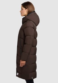 Manteau en duvet marron avec capuche, présentant un design matelassé, des poches latérales zippées et un col côtelé, fabriqué dans un tissu lisse et mat.