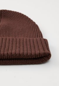 Béret en tricot marron avec une texture côtelée et un revers replié. Le matériau doux présente une couleur chaude et uniforme.