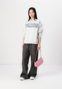 Felpa grigia con stampa "PARIGI", abbinata a pantaloni larghi grigi scuri, sneakers bianche e una piccola borsa a tracolla rosa.