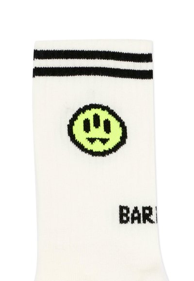 Chaussette blanche avec deux bandes noires en haut, un visage souriant à trois yeux de couleur vert néon, et un texte noir partiellement visible "BAR" près du bord-côte.
