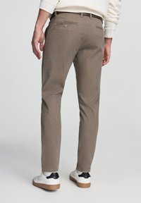 Pantaloni khaki in twill con una vestibilità slim, caratterizzati da due tasche posteriori e una superficie testurizzata. Abbinati a sneaker bianche e dettagli neri sui tacchi.