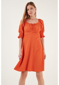Orange, textured dress with a square neckline and ruched detailing, featuring puff sleeves and smocked cuffs, flowing to a knee-length hem.