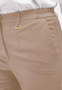 Beige op maat gemaakte broeken met een gladde textuur, voorzien van een elastische tailleband, een gouden accenthardware lus en zijzakken.