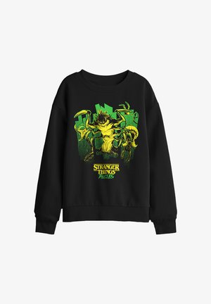 Black sweatshirt with yellow-green monster graphic and cityscape background, featuring "Stranger Things Tales from 85" text below.