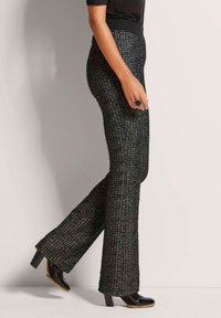 Zwarte en patroon brede broek gemaakt van textuurstof; heeft een aansluitende tailleband en wordt gedragen met glanzende zwarte hoge hakken.