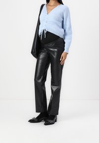 Maglione lavorato a maglia blu chiaro con cordino frontale, abbinato a pantaloni in ecopelle nera a vita alta e scarpe nere con punta e dettagli argentati.