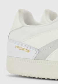 Baskets blanches de sport avec une tige en maille texturée, des accents en daim et une semelle en caoutchouc avec un motif en losange. "PREDATOR" est imprimé en doré.
