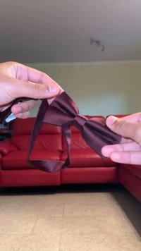 Papillon in raso marrone tenuto tra due mani, caratterizzato da una forma classica con una texture liscia e una cinghia regolabile per la chiusura.