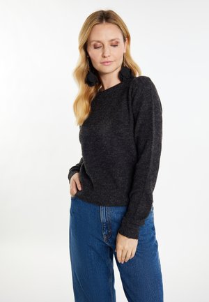 Pulover negru cu textură, cu o croială lejeră și manșete cu nervuri, purtat cu blugi largi de culoare bleu deschis, cu talie înaltă.