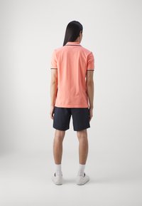 Rožinė polo marškinė su juodu apvadu, suderinta su tamsiai mėlynomis šortais. Balti sportbačiai ir kojinės užbaigia įvaizdį. Minimalistinis, kasdienis dizainas.