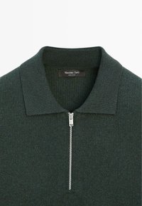 Tmavě zelený polo svetr na zip s texturovaným úpletem, s plochým límcem a stříbrným zipem jako detailem. Uvnitř límce je viditelná značka značky.