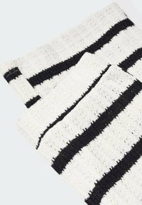 Shorts en tricot blancs avec de larges rayures horizontales noires, pliés sur un fond clair.