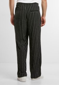 Pantaloni cu dungi alb-negru, dintr-un material texturat, având un design cu picior larg și un buzunar la spate cu închidere prin buton.