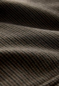 Brauner strukturierter Stoff mit einem Fischgrätmuster und dunklen Streifen, weiche und leicht flauschige Oberfläche, die komplexe Webdetails zeigt.