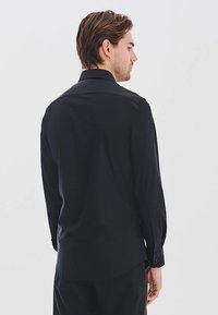 Czarna koszula z długim rękawem, z kołnierzykiem, o gładkiej fakturze i zapinanych mankietach. Krój nieco dłuższy z tyłu. Minimalistyczny design, bez wzorów.