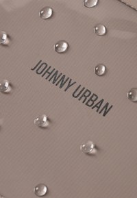 Tessuto beige texture con gocce d'acqua e il nome del marchio "JOHNNY URBAN" stampato in grassetto nero.