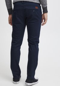 Chinos de algodón azul marino con un corte ajustado, que cuentan con dos bolsillos traseros con botones y un pequeño parche de cuero marrón en la cinturilla.