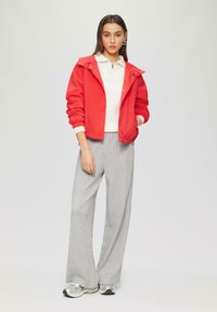 Raudona lengva striukė su kapišonu, derinama su balta raiščia ganas piko viršuje, pilkai languotais plačiais kelnais ir sidabriniais sportbačiais.