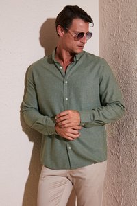 Camisa verde de botones con un tejido texturizado, de mangas largas y botones claros, combinada con pantalones beiges. Lleva unas gafas de sol.