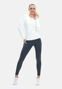 Weißes langärmliges Sportshirt, kombiniert mit dunkelgrauen Leggings und weißen Sneakers, mit slim fit und glatter Stofftextur.